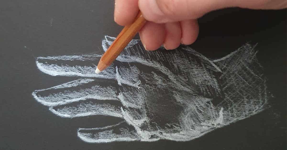 A hand drawing a hand on black paper with white charcoal